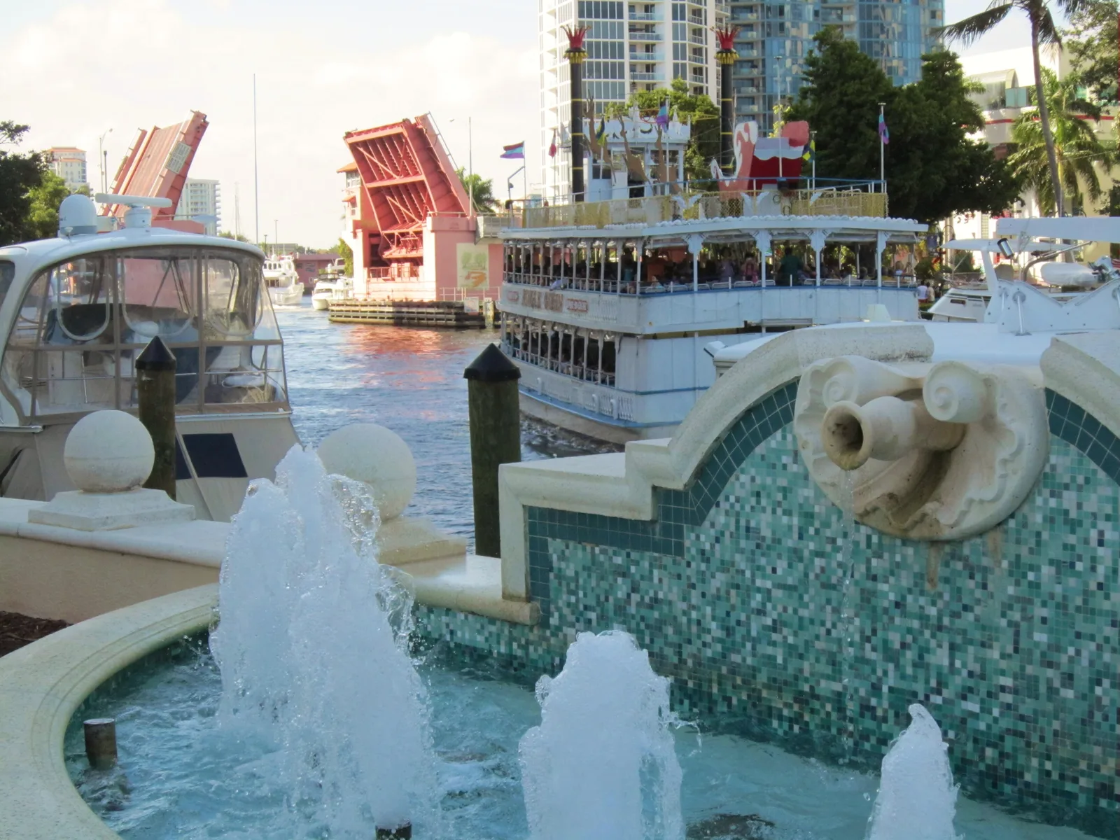 A fountain on the Riverwalk beside the New River in downtown Fort Lauderdale, with a drawbridge raised behind.